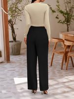 Person wearing a beige top and black pants in an indoor setting with wooden chairs and plants.