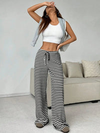 Person wearing a white crop top and black and white striped pants in a living room.