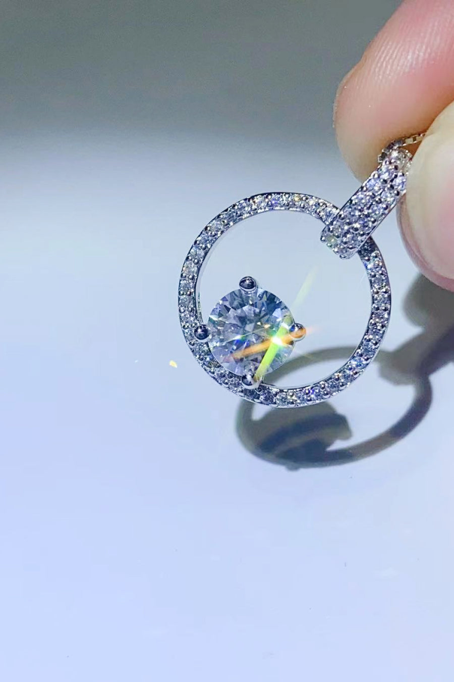 Close-up of a diamond ring held by a hand on a light gray background