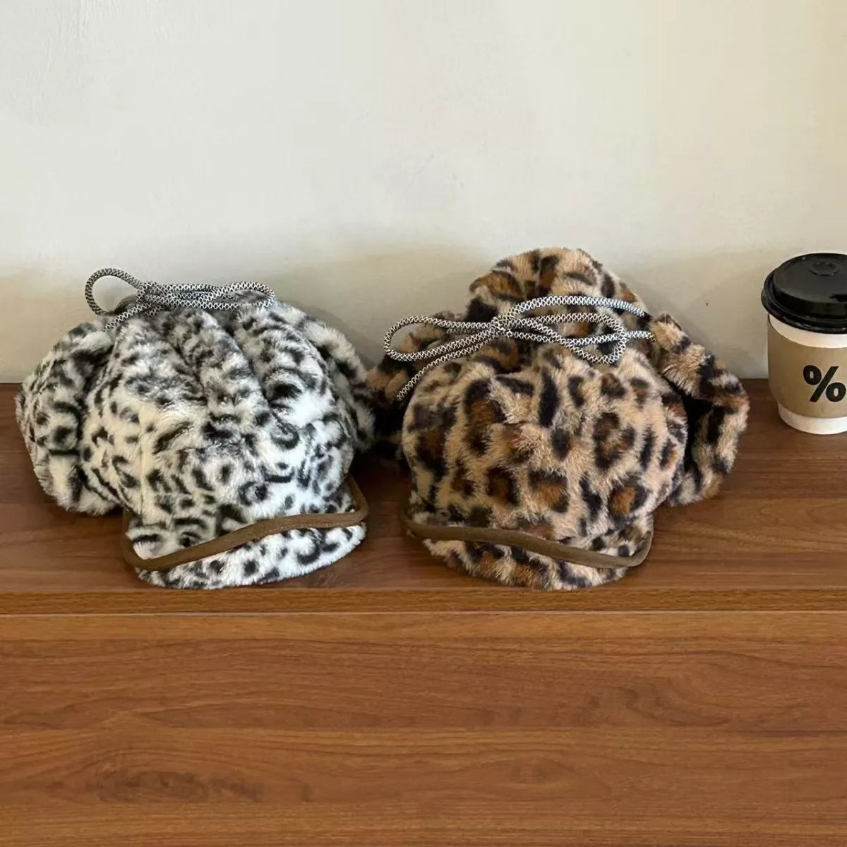 Two leopard print drawstring bags on a wooden surface with a coffee cup in the background.