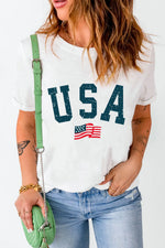 Person wearing a white t-shirt with 'USA' and an American flag graphic, holding a green purse.