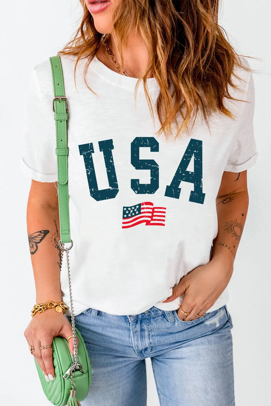Person wearing a white t-shirt with 'USA' and an American flag graphic, holding a green purse.