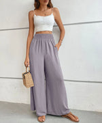 Woman wearing a white crop top and light purple wide-leg pants against a plain background
