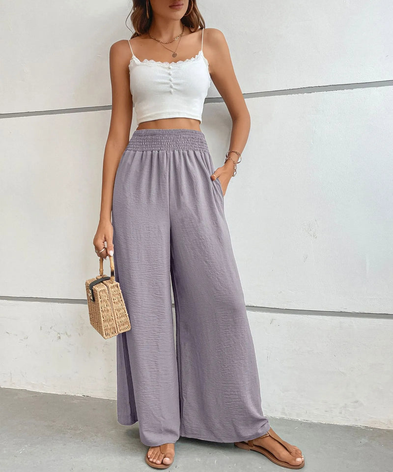 Woman wearing a white crop top and light purple wide-leg pants against a plain background