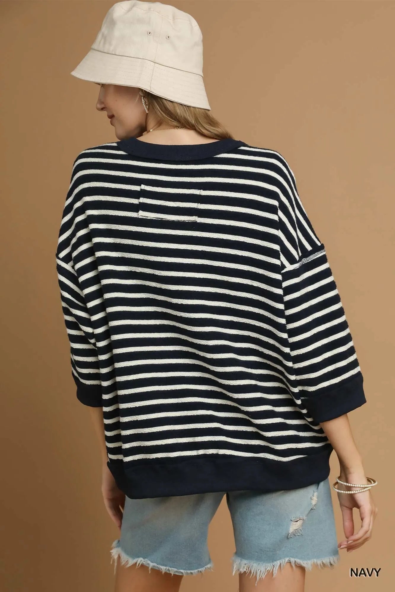 Person wearing a navy and white striped sweater with denim shorts on a brown background