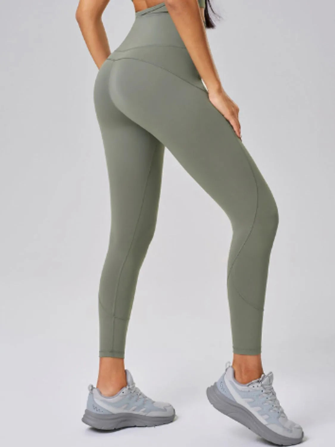Person wearing green leggings and gray sneakers on a light gray background