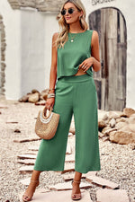 Woman in a green outfit standing on a stone path with rocks and a white wall in the background.