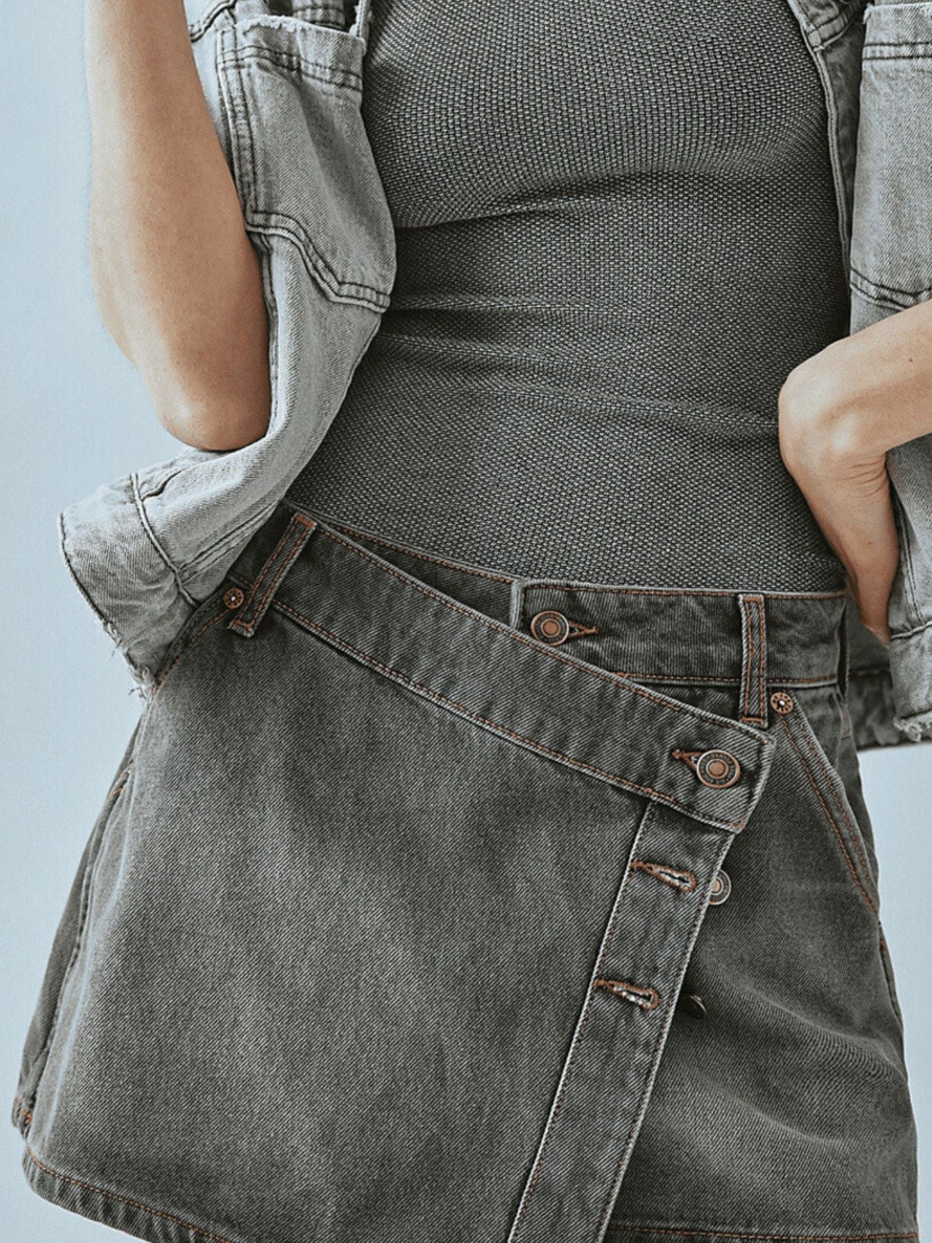 Person wearing a gray denim apron over a black top against a light blue background