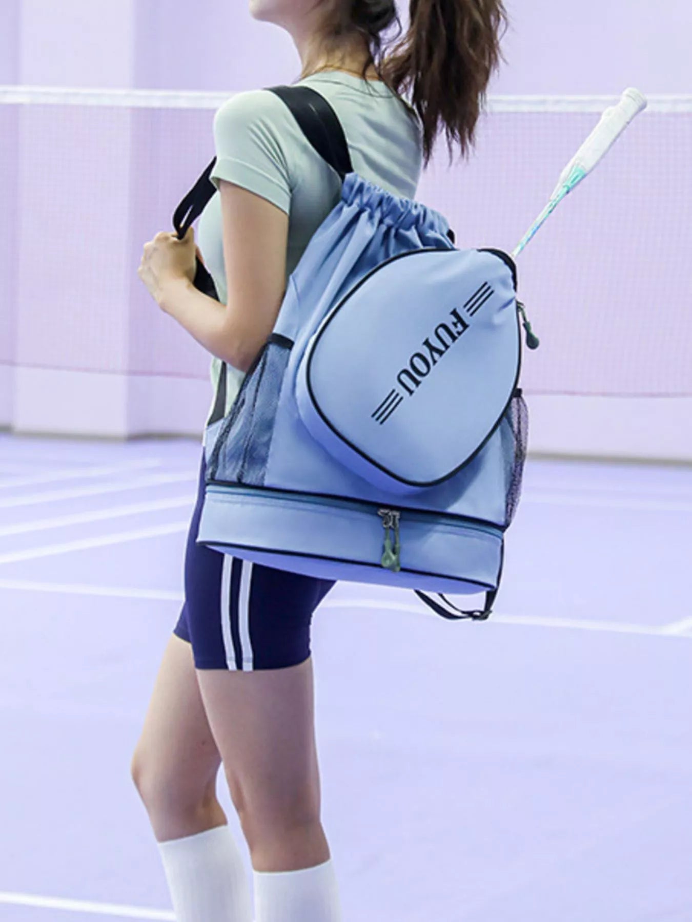 Person holding a blue backpack with 'Fy vou' branding on a tennis court.