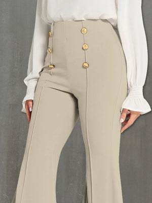 Beige pants with gold buttons worn by a person against a gray background