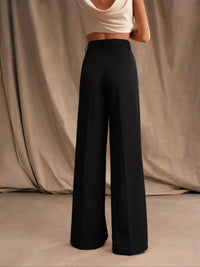 Person wearing black wide-leg pants and a white top against a beige curtain background