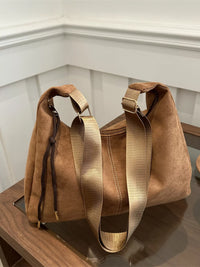 Brown suede handbag with beige straps on a wooden surface.
