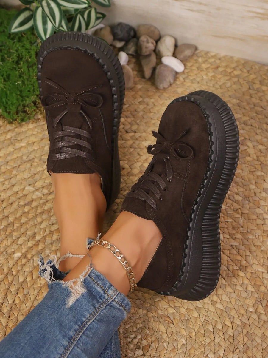 Brown suede shoes with thick soles worn by a person on a textured surface.