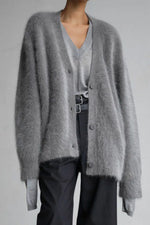 Person wearing a gray cardigan over a light gray shirt with dark pants on a plain background