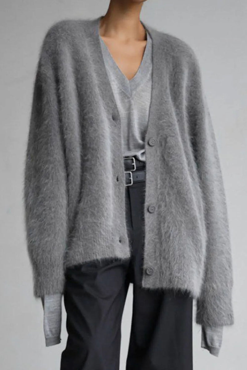 Person wearing a gray cardigan over a light gray shirt with dark pants on a plain background