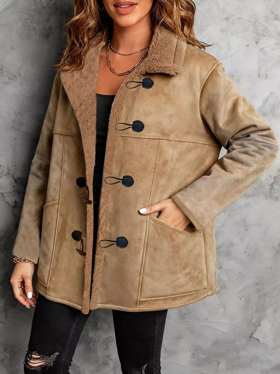 Woman wearing a beige shearling coat with black buttons against a gray background