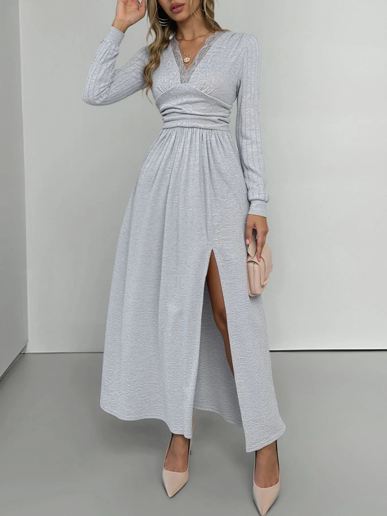 Woman wearing a gray long-sleeve dress with a slit on a plain background
