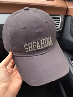 Gray cap with 'SHGAHINA' text held inside a car.