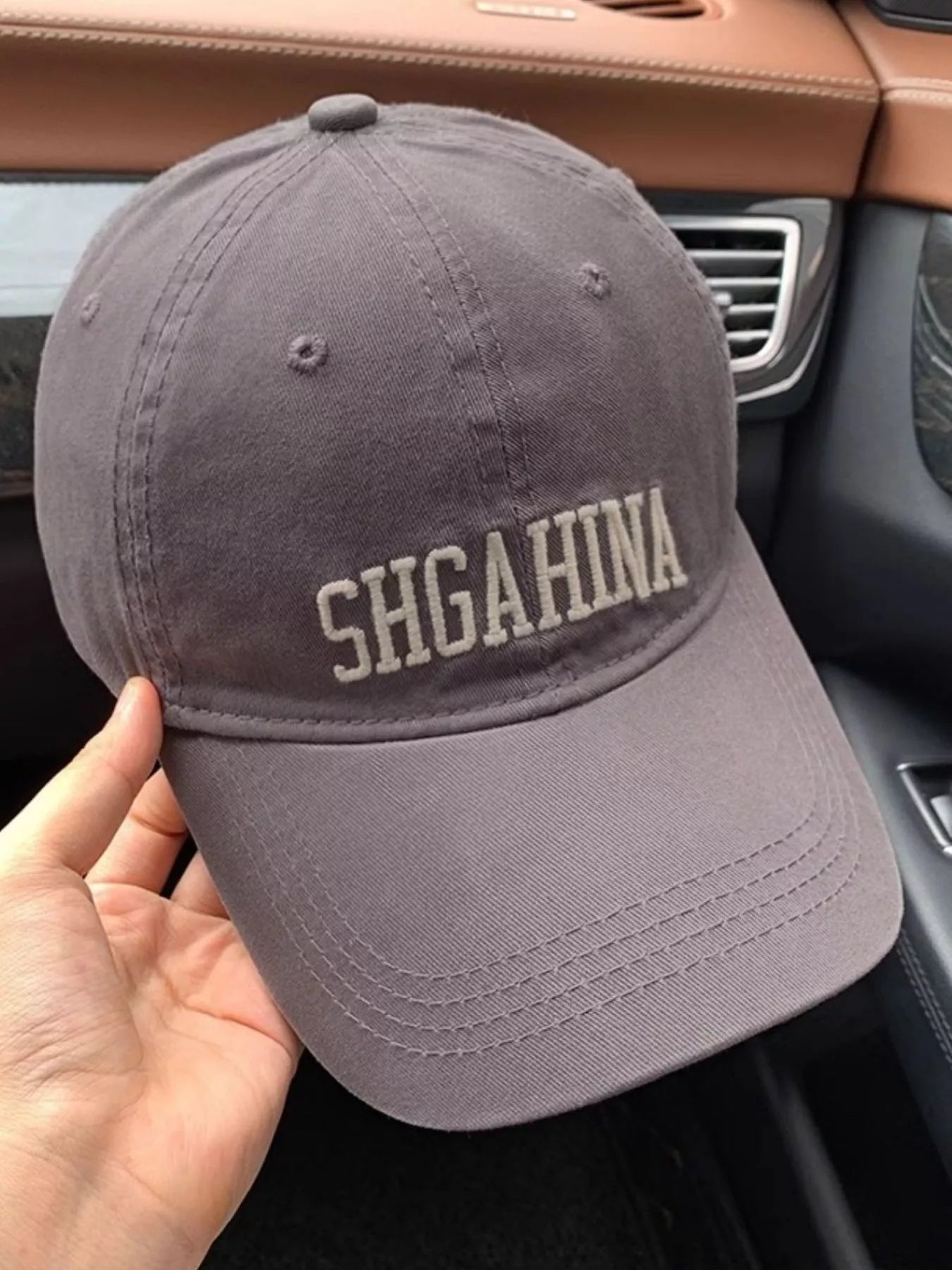 Gray cap with 'SHGAHINA' text held inside a car.