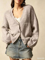 A woman wearing a light gray knit cardigan with a V-neck and button closure, paired with a denim mini skirt, against a neutral beige background.