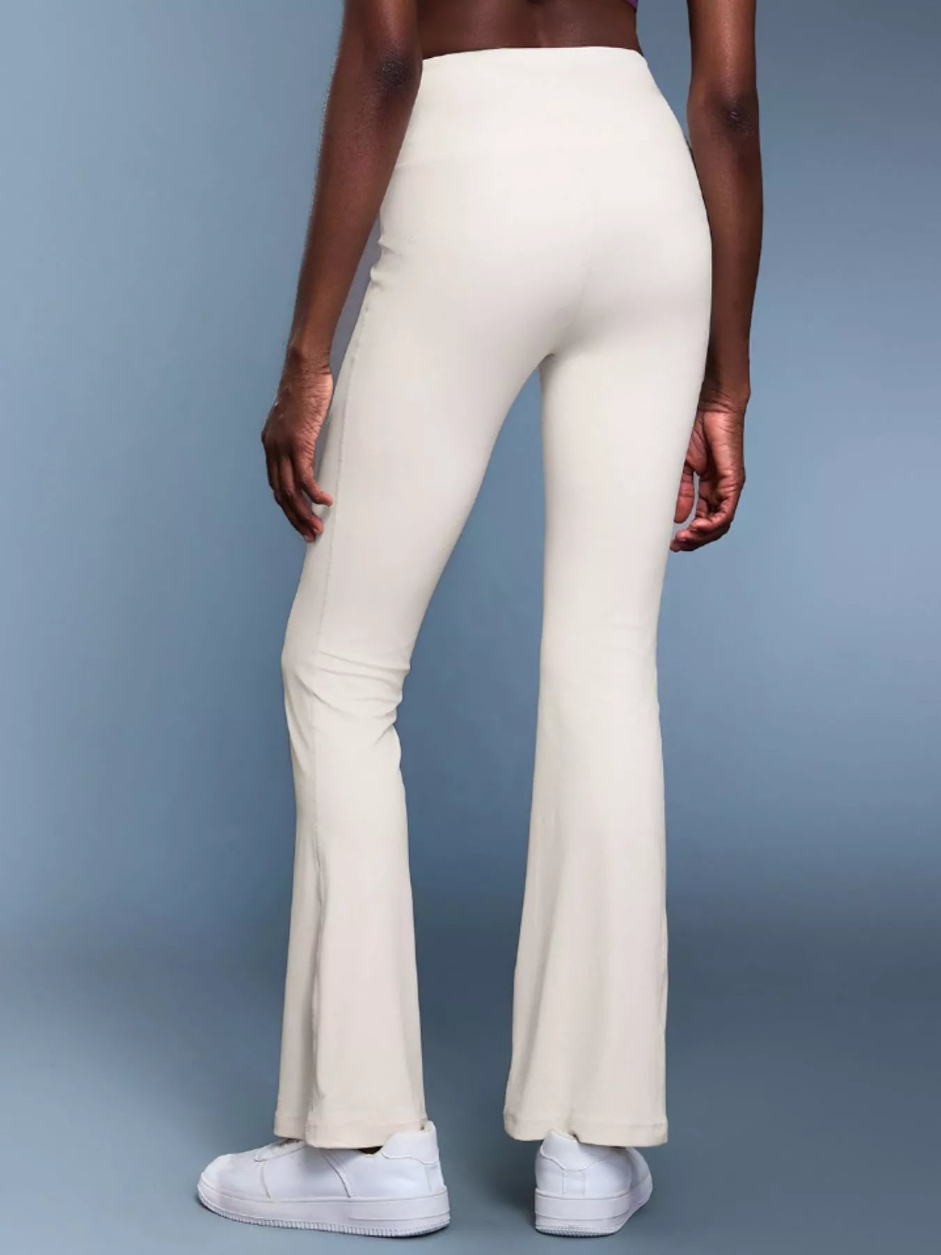 Person wearing white flared pants on a gray background