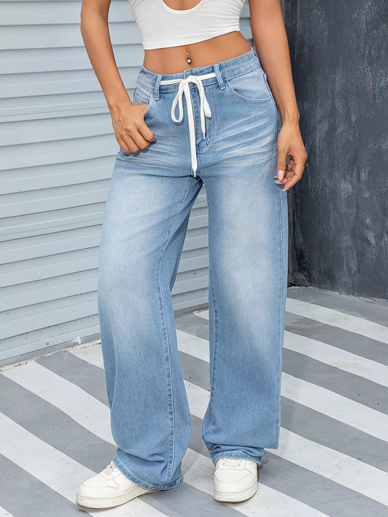 Person wearing light blue jeans with a white top on a striped floor.