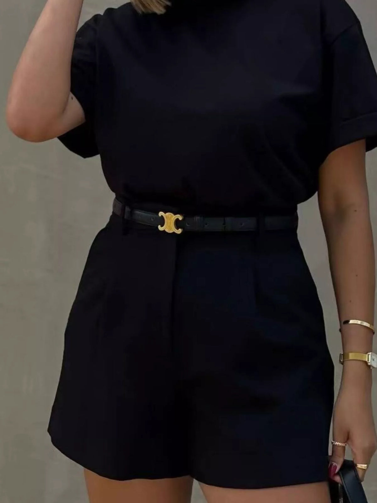 Person wearing a black outfit with a belt against a neutral background