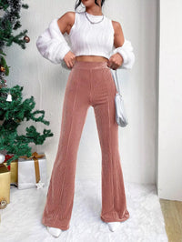Person wearing a white top and brown ribbed pants in a festive setting with a Christmas tree.
