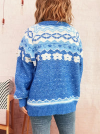 Person wearing a blue knitted sweater with a pattern, standing against a light-colored wall.