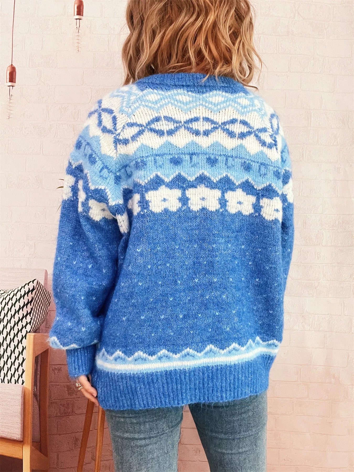 Person wearing a blue knitted sweater with a pattern, standing against a light-colored wall.