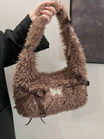 Brown fluffy handbag with a bow held by a person against a neutral background