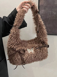 Brown fluffy handbag with a bow held by a person against a neutral background