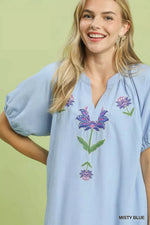 Woman wearing a light blue blouse with floral embroidery on a green background