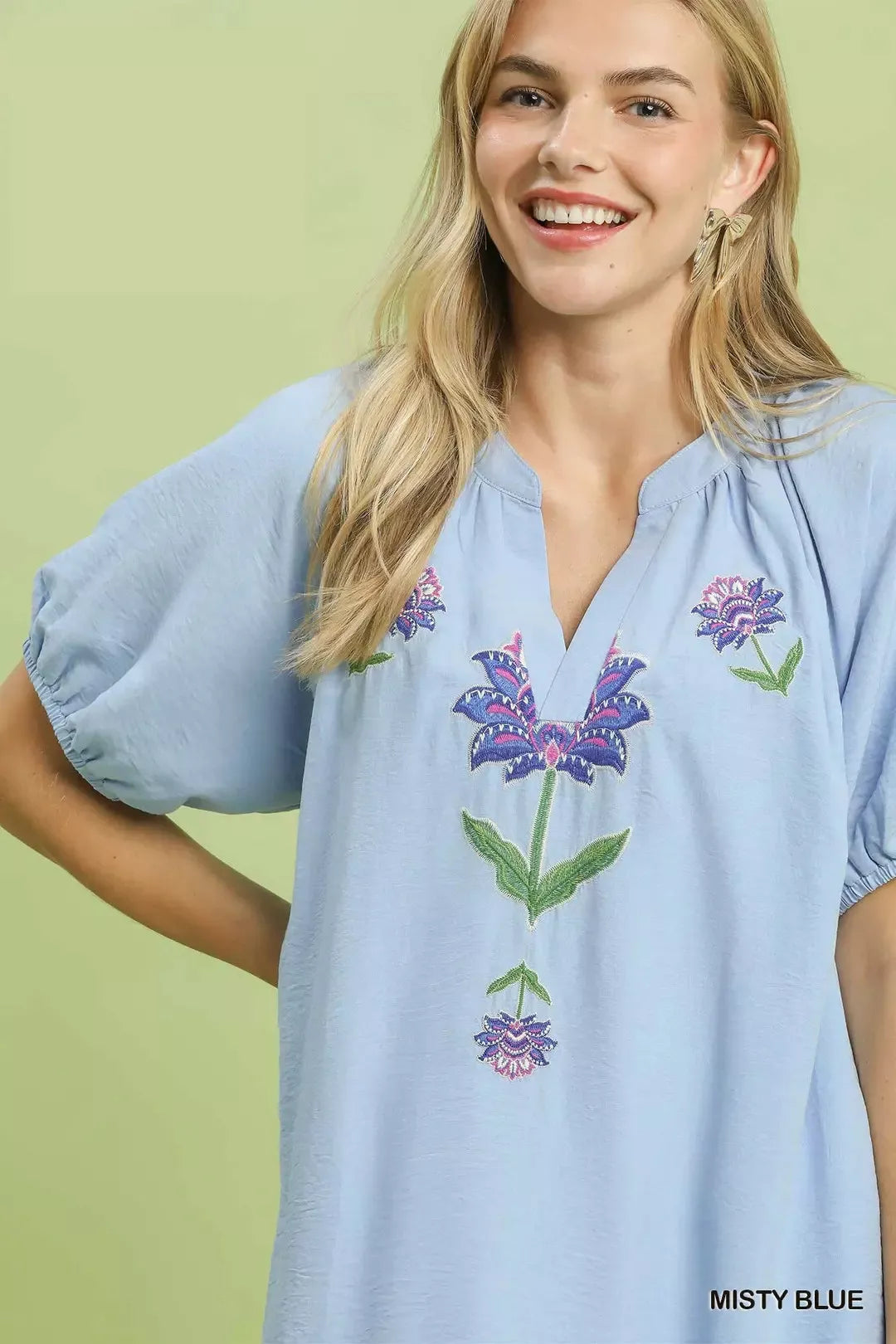 Woman wearing a light blue blouse with floral embroidery on a green background