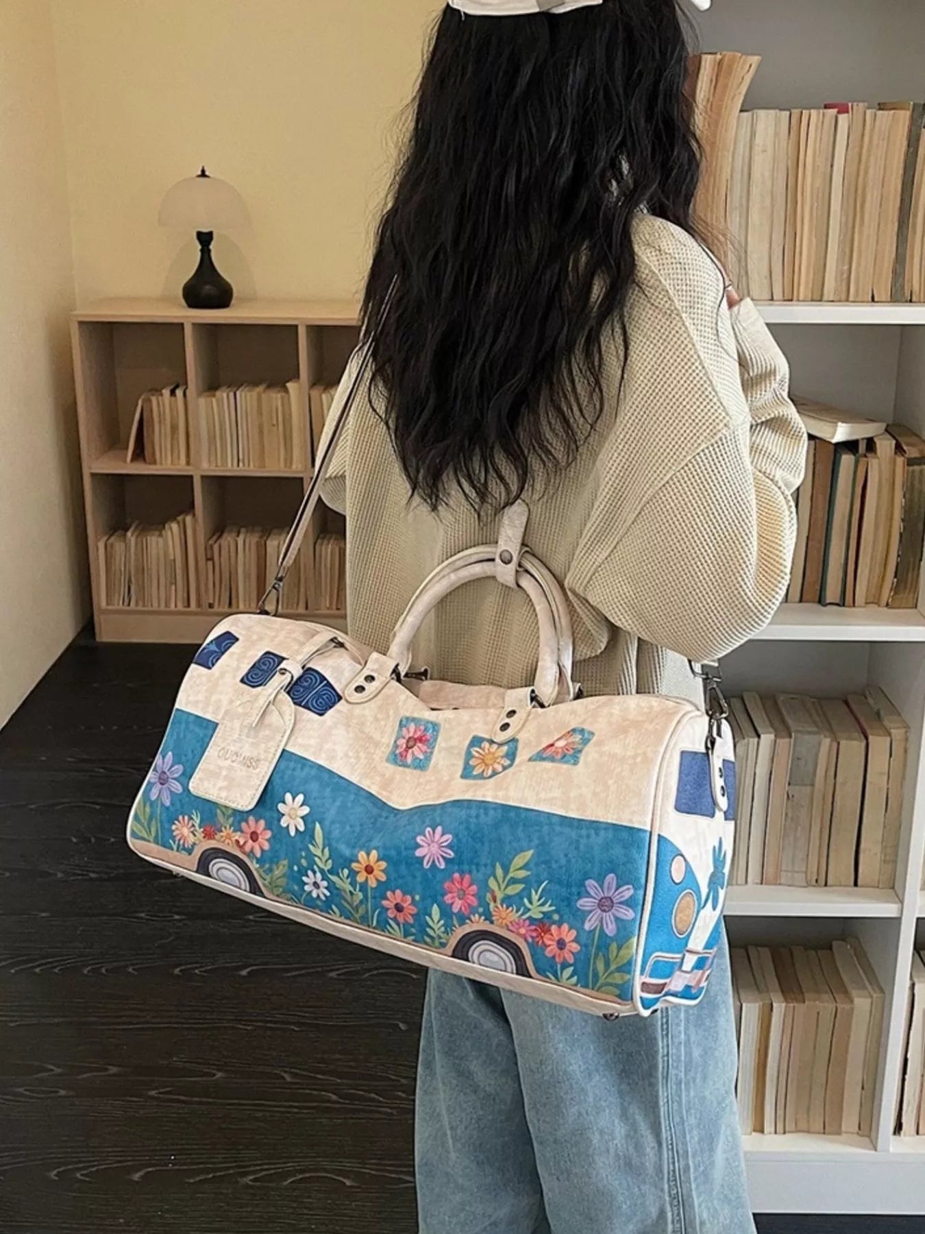 Person holding a floral-patterned duffel bag in a room with bookshelves.