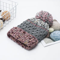 Knitted hat with pom-pom and scarf on a white surface with yarn balls and a basket in the background.