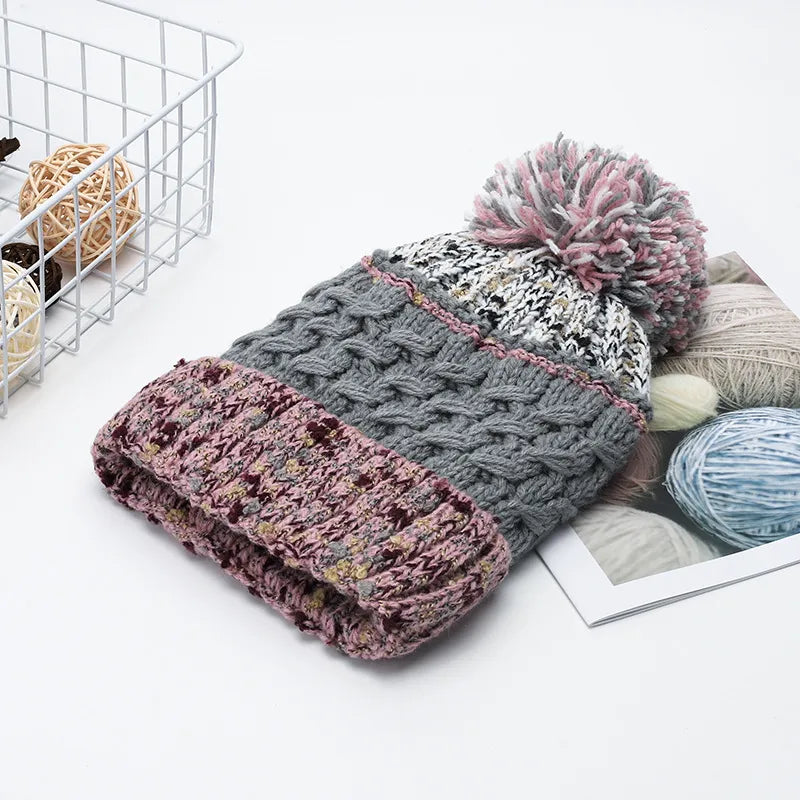Knitted hat with pom-pom and scarf on a white surface with yarn balls and a basket in the background.