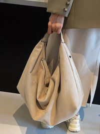 Person holding a beige handbag with a neutral background