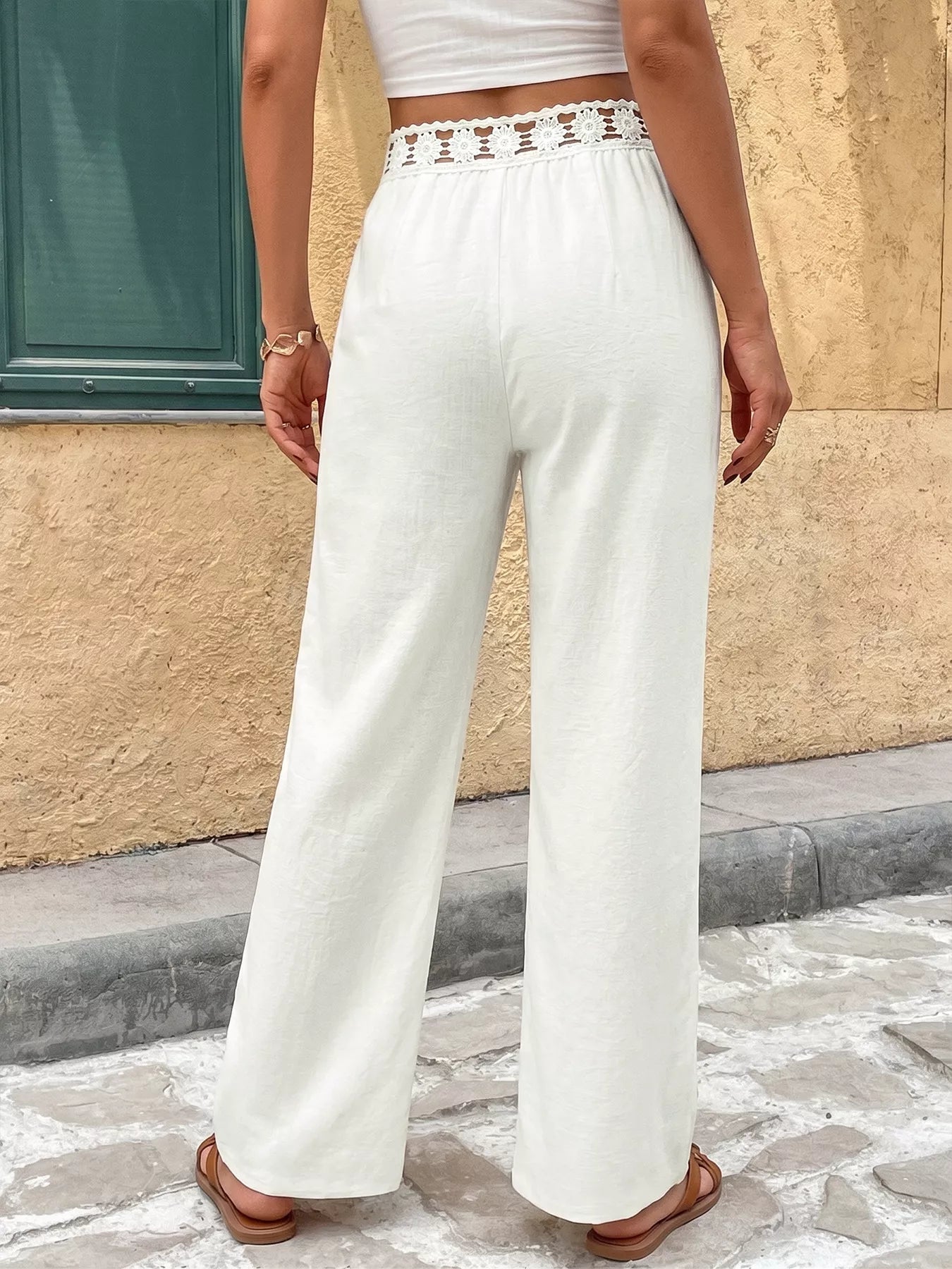 Person wearing white pants with lace waistband standing against a beige wall.