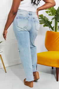 Person wearing light blue jeans standing in a room with a yellow chair and plant.