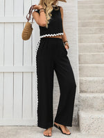 Woman wearing a black outfit with white trim standing against a white wall.