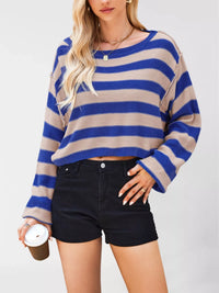 Person wearing a blue and beige striped sweater with black shorts on a plain background