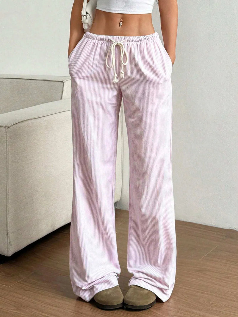 Person wearing light pink striped pajama pants in a room with a beige couch.