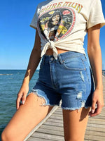 Person wearing a graphic t-shirt and denim shorts by the ocean