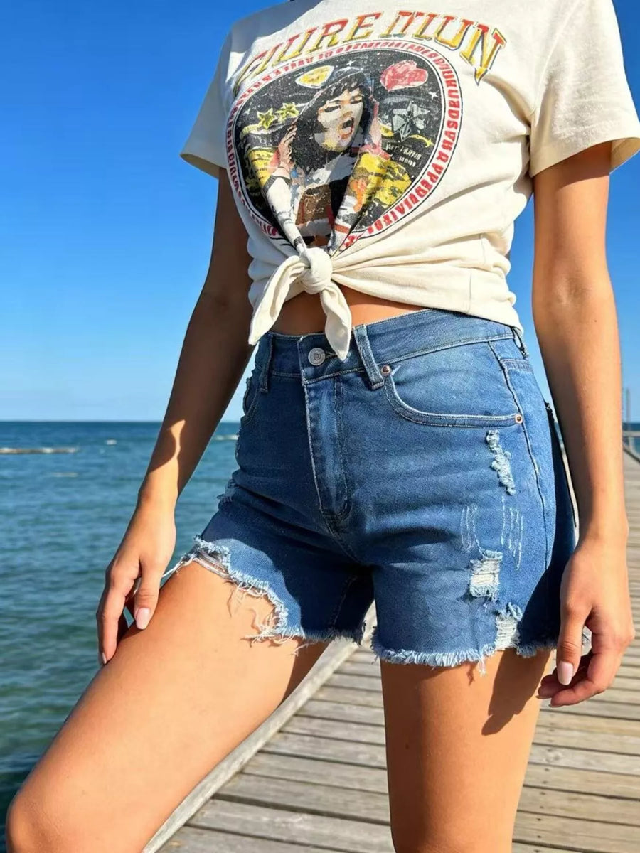 Person wearing a graphic t-shirt and denim shorts by the ocean