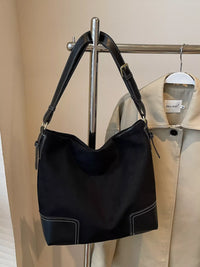 Black handbag on a metal stand with beige jacket in the background