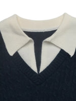 Close-up of a knit sweater with a dark navy body and a contrasting cream collar, showing the ribbed texture and V-neckline.