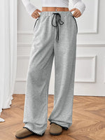 Person wearing gray sweatpants with a white top and brown shoes on a wooden floor.