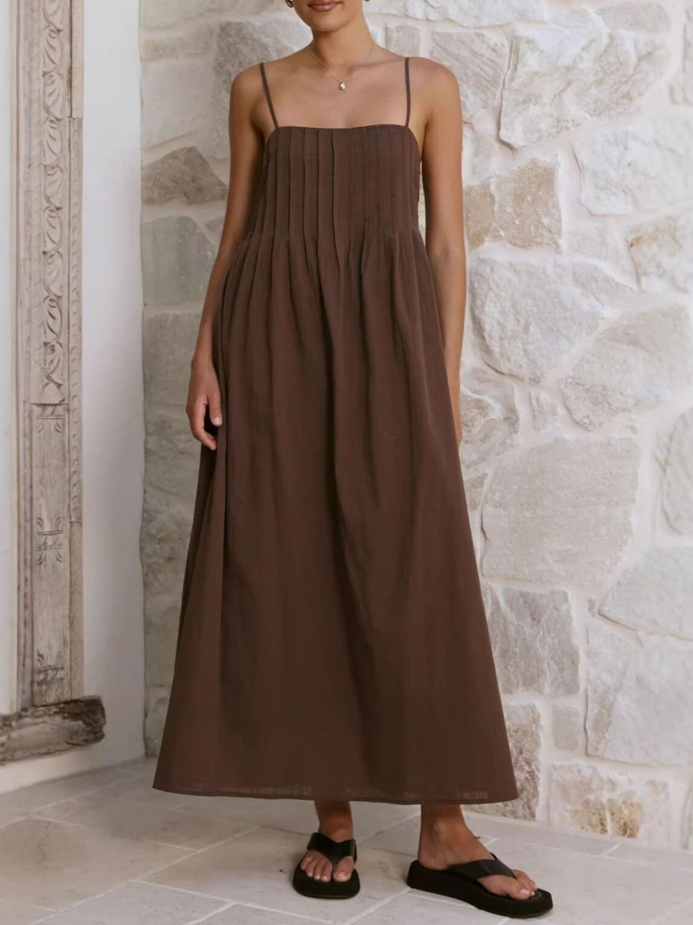 Woman wearing a brown dress standing against a stone wall.