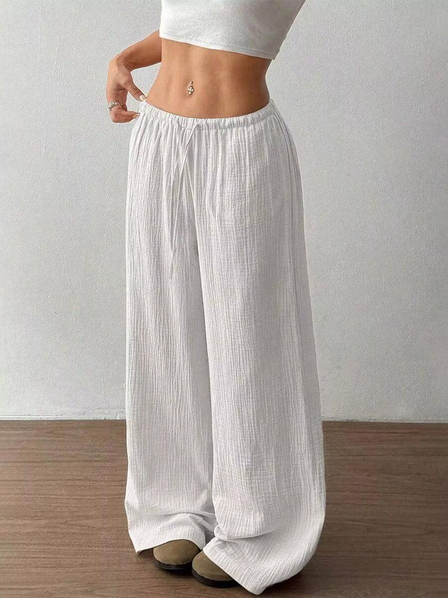 Person wearing white wide-leg pants and a white top against a plain background